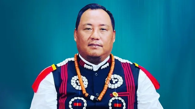 Formal portrait of Benjamin Yepthomi in a traditional Naga waistcoat and bead necklace against a deep teal background.
