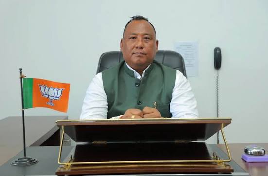 Benjamin Yepthomi seated at an office desk with a Bharatiya Janata Party desk flag beside him.