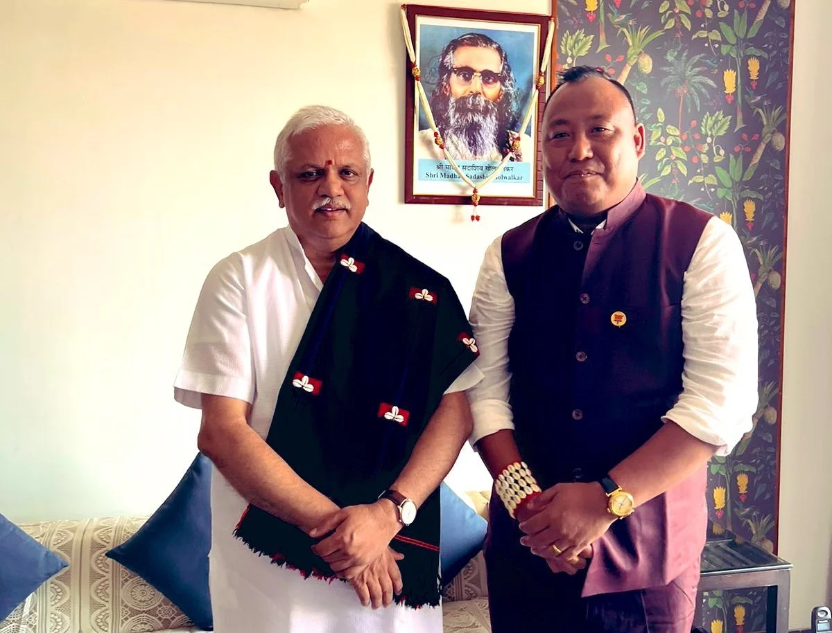 Benjamin Yepthomi standing beside a senior national party leader wearing a Naga shawl, at an indoor meeting.