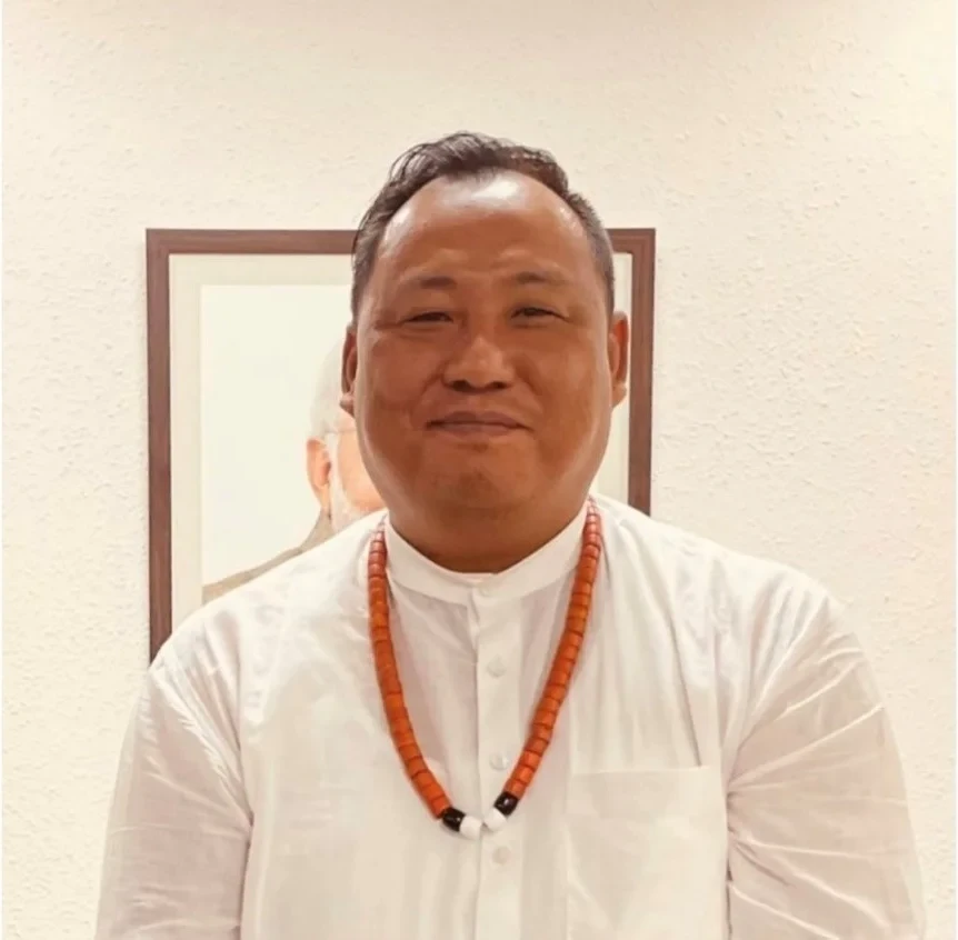 Portrait of Benjamin Yepthomi, State President of the Bharatiya Janata Party in Nagaland, in a white shirt with a traditional Naga bead necklace.