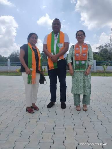 Benjamin Yepthomi standing between two party workers wearing BJP scarves on a paved forecourt, photographed in September 2023.