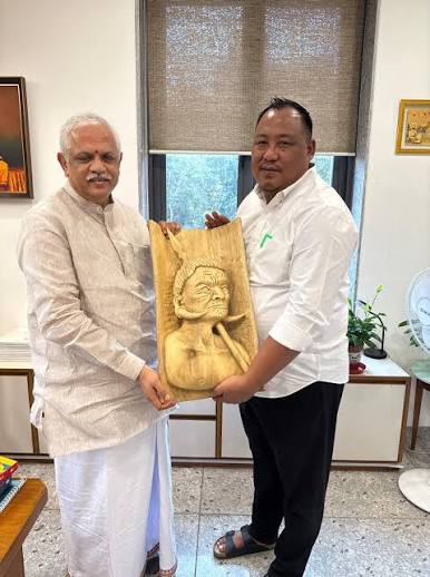 Benjamin Yepthomi holding a carved wooden Naga panel together with a senior party leader in an office interior.