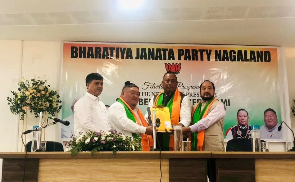 Benjamin Yepthomi being felicitated on stage beneath a Bharatiya Janata Party Nagaland banner, receiving a memento from party colleagues wearing BJP scarves.